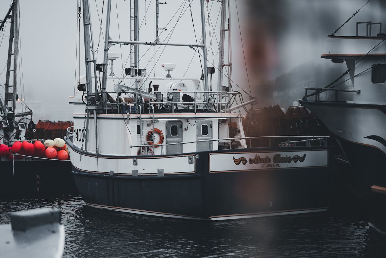 A moored fishing boat in a misty harbor with colorful buoys on a foggy day.